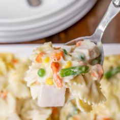 a spoon full of pasta and vegetables on a white plate with a fork in it