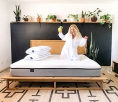 a woman standing on top of a bed in a room with plants and potted plants