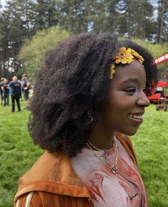 a woman with an afro and flower in her hair smiles at the camera while standing on grass