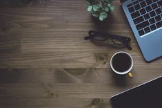 a laptop computer sitting on top of a wooden table next to a cup of coffee