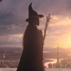 a woman in a witch costume holding a broom on top of a hill at sunset