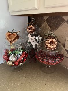 three glass bowls filled with candies on top of a counter next to white cabinets