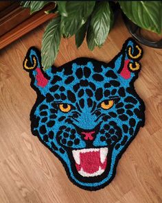 a blue rug with a black and red leopard head on the floor next to a potted plant