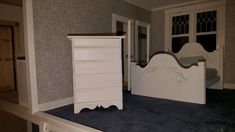 a white dresser sitting on top of a blue carpeted floor next to a bed