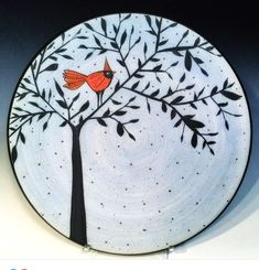 a white plate with a red bird sitting on it's side and tree painted on the front