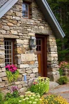 a stone house with flowers in front of it and a wooden door on the side