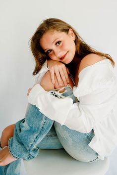 a young woman sitting on top of a white toilet wearing jeans and a white shirt