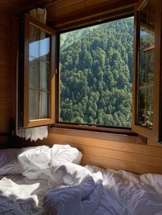 an unmade bed sitting in front of a window on top of a wooden wall