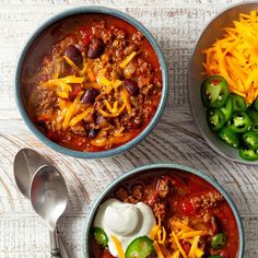 three bowls of chili with cheese, sour cream and jalapenos on the side