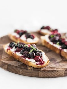 several pieces of bread with berries and cream on them sitting on a wooden cutting board