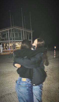 two people hugging each other in front of a building at night with the lights on