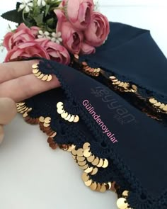 a person holding onto a black cloth with gold sequins and flowers in the background