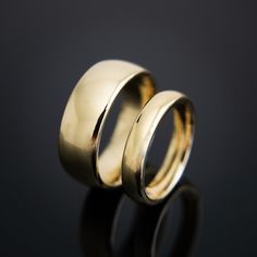 two gold wedding rings sitting side by side on a black surface with reflections in the background