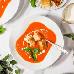 a bowl of tomato soup with croutons and spinach leaves on the side