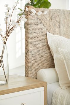 a vase with white flowers sitting on top of a bed next to a pillow and blanket