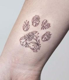 a dog paw tattoo with flowers and butterflies on the left side of the wrist area