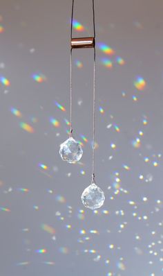 two clear glass bubbles hanging from a metal bar on a string with rainbow colored lights in the background