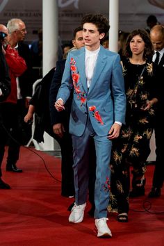 a man in a blue suit and white shirt walking down a red carpeted area