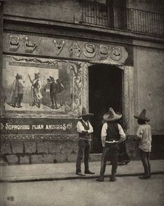 two men standing in front of a building with an advertisement on the wall behind them