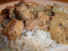 a white plate topped with rice and meat covered in gravy on top of a wooden table