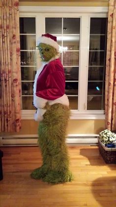 a man in a costume standing next to a window wearing a santa claus hat and green pants