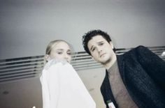 a man and woman standing next to each other in front of a window with blinds