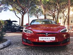 a red car is parked in front of some trees