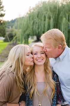 two women and a man kissing each other in front of some willow trees on a sunny day