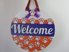 a welcome sign hanging from the side of a wall with paw prints and purple ribbon