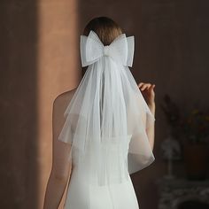 a woman wearing a white veil with a bow on it's head is standing in front of a wall