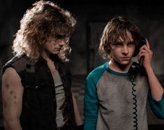 two young men standing next to each other talking on telephones