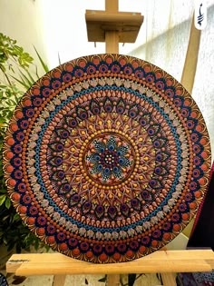 a wooden easel holding a colorfully designed plate on it's stand in front of a wall