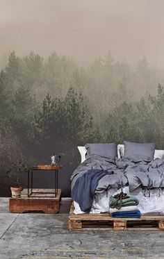 a bed sitting on top of a wooden pallet in front of a forest wall