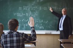 two men standing in front of a blackboard with their hands up to the sky