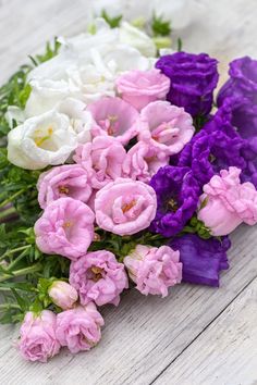 purple, white and pink flowers are laying on the floor together in a bouquet with green leaves