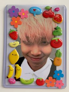 a young man with pink hair and fruit magnets in front of him is smiling at the camera