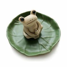 a ceramic frog sitting on top of a leaf shaped plate with eyes wide open and one eye partially closed