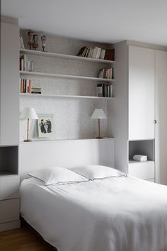 a white bed sitting in a bedroom next to a book shelf