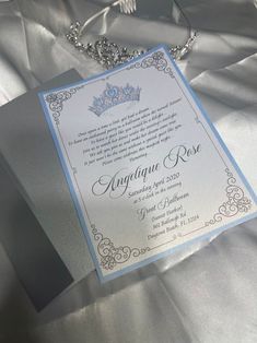 a wedding card with a tiara on it sitting on a silver satin table cloth