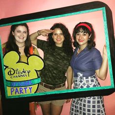 three women posing for a photo in front of a mickey mouse sign with the disney channel logo on it