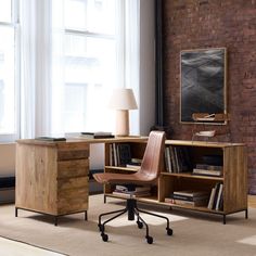 an office with a desk, chair and bookshelf in front of a brick wall