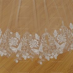 a white lace with flowers and birds is on a wooden floor next to a piece of cloth