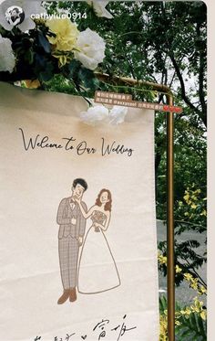 a welcome to our wedding banner hanging on a pole with flowers in the back ground