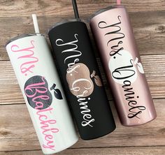 three personalized tumblers with straws in them on a wooden surface, one is pink and the other is black