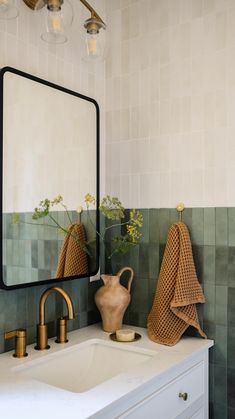 a white sink sitting under a bathroom mirror next to a vase with flowers in it