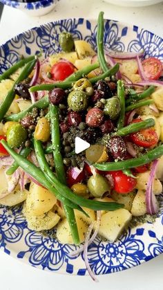 a blue and white plate topped with green beans, olives, tomatoes and potatoes