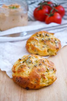 two muffins sitting on top of a wooden cutting board next to some tomatoes