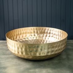 a large metal bowl sitting on top of a cement floor next to a blue wall