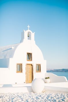 a white building with a cross on the top and water in the backround