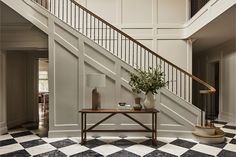 a foyer with black and white checkered flooring, two vases on a table next to the staircase